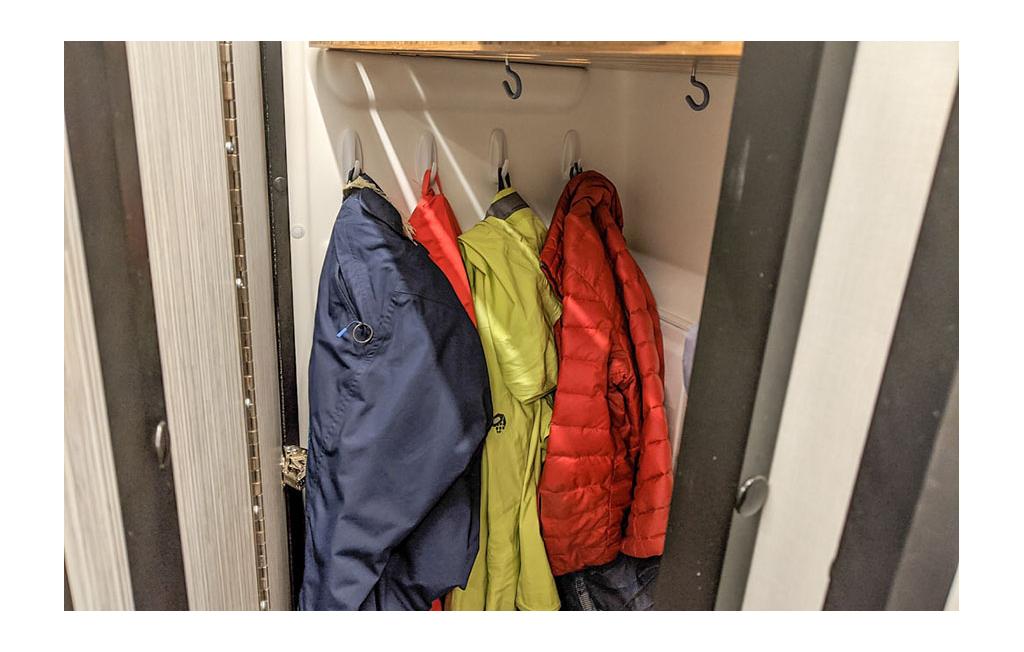 Hooks on the wall in the bathroom with snow pants and jackets hanging from them.