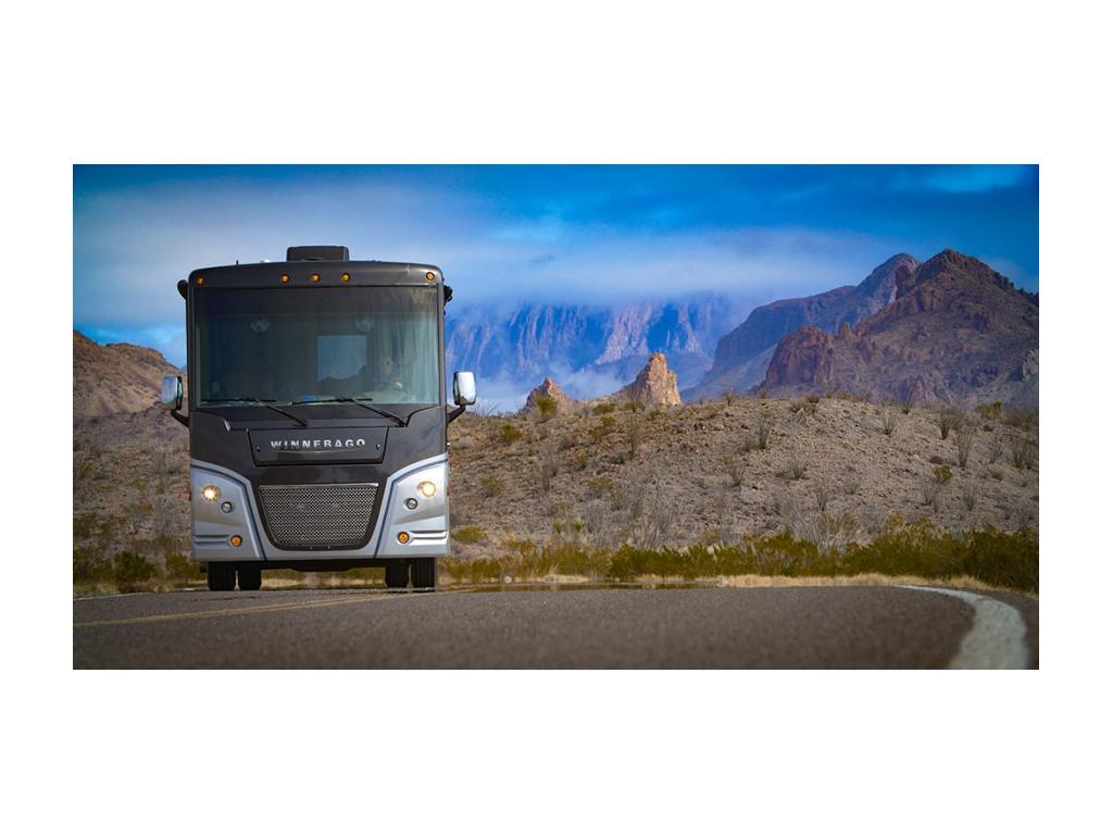 Adventurer driving down road with mountains and blue sky in background