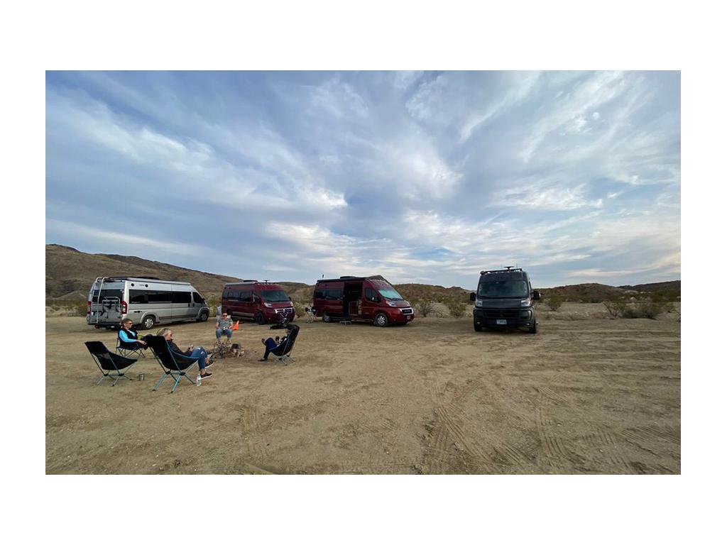 Four people sitting in camp chairs in a circle with four Travatos in background
