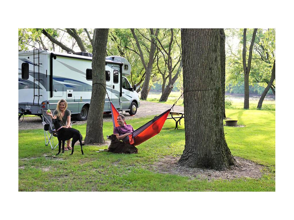 Lindsay sitting in chair throwing ball to large black dog. Dan is sitting in a red hammock next to a large brown and white dog. Navion is parked behind them