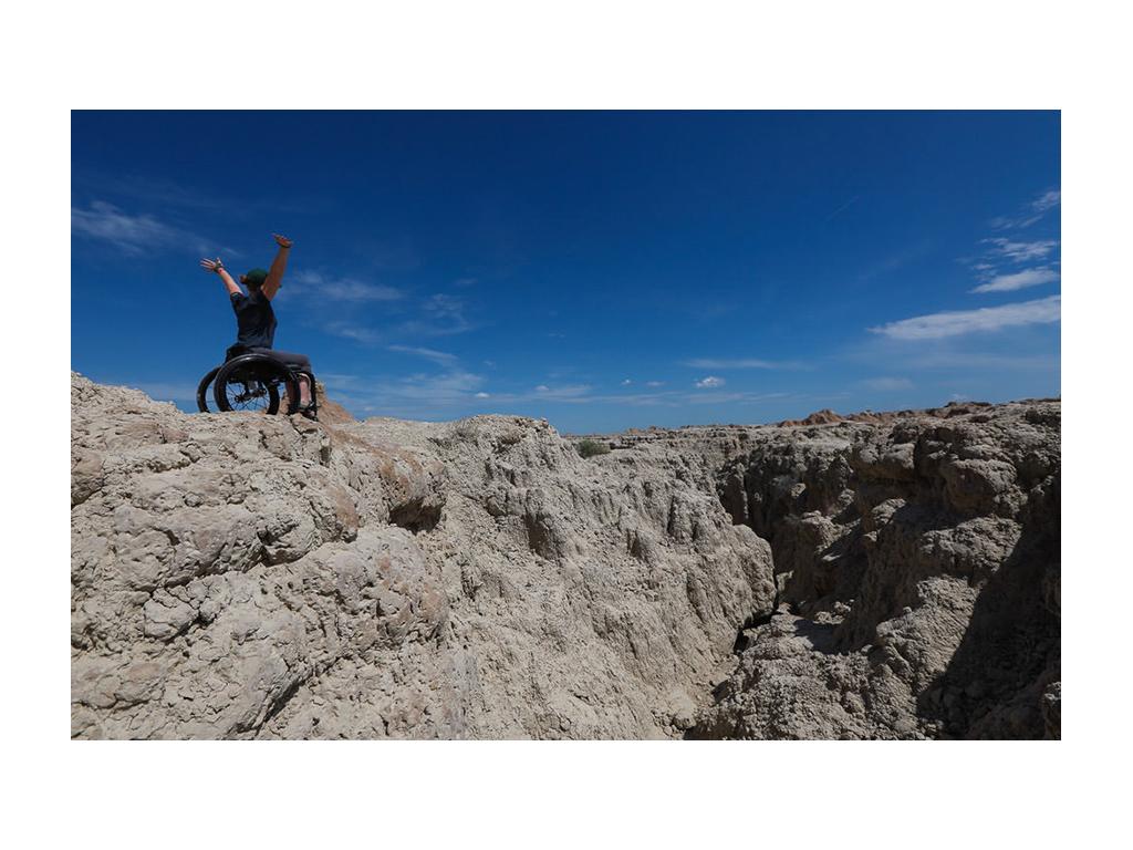 Nerissa at No Barriers with arms thrown up in air on top of a mountain