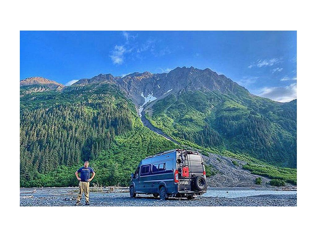 Nick Riebe standing next to Travato with green mountains in the background
