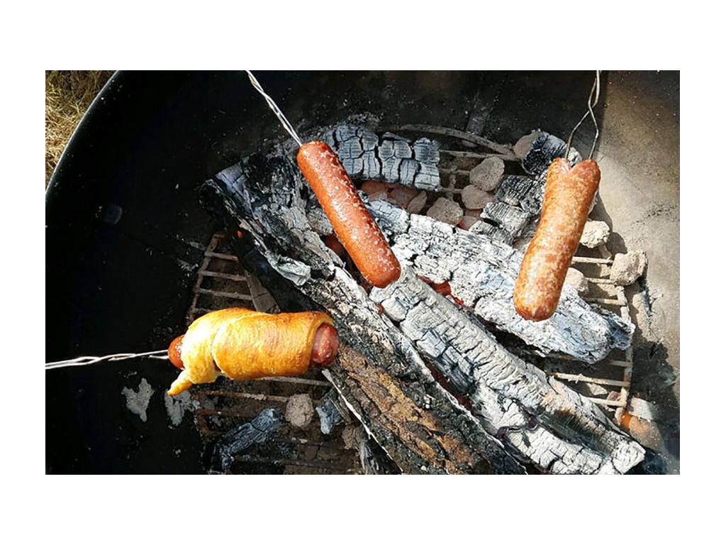 Three hot dogs on sticks roasting over campfire. One hot dog is wrapped in a crescent roll
