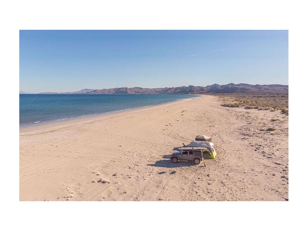 Jeep parked on beach next to two tents