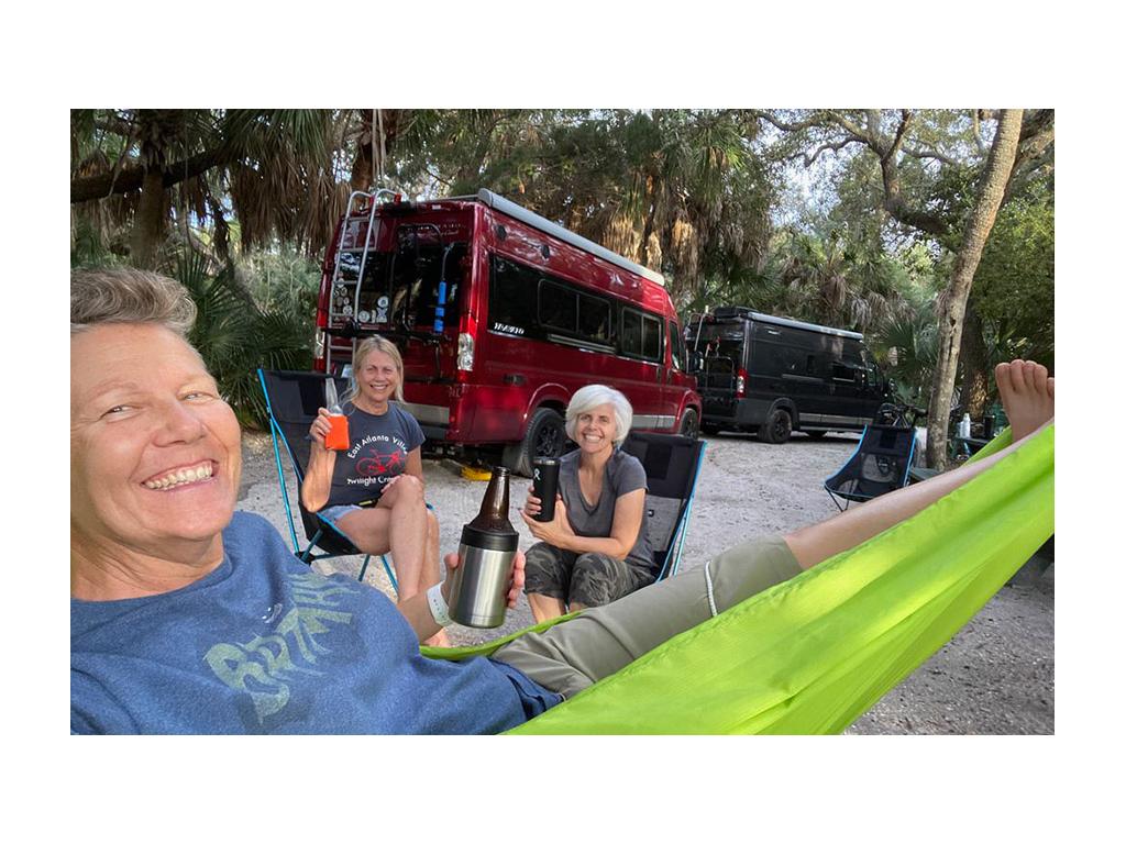 Chris and friend sitting in chairs next to Noel in hammock. Two Travatos are parked in the background