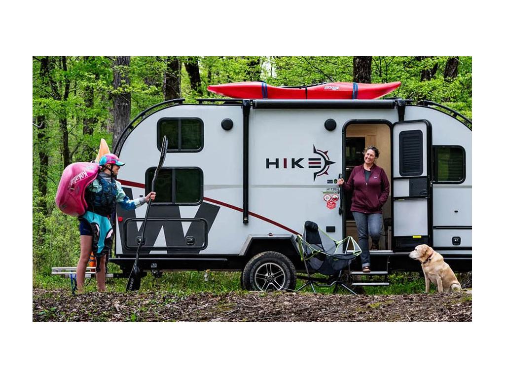 Kathy Holcombe standing in doorway of Winnebago Hike smiling at Abby Holcombe who is carrying kayak and paddle. Their yellow lab, Tucker, is sitting nearby.