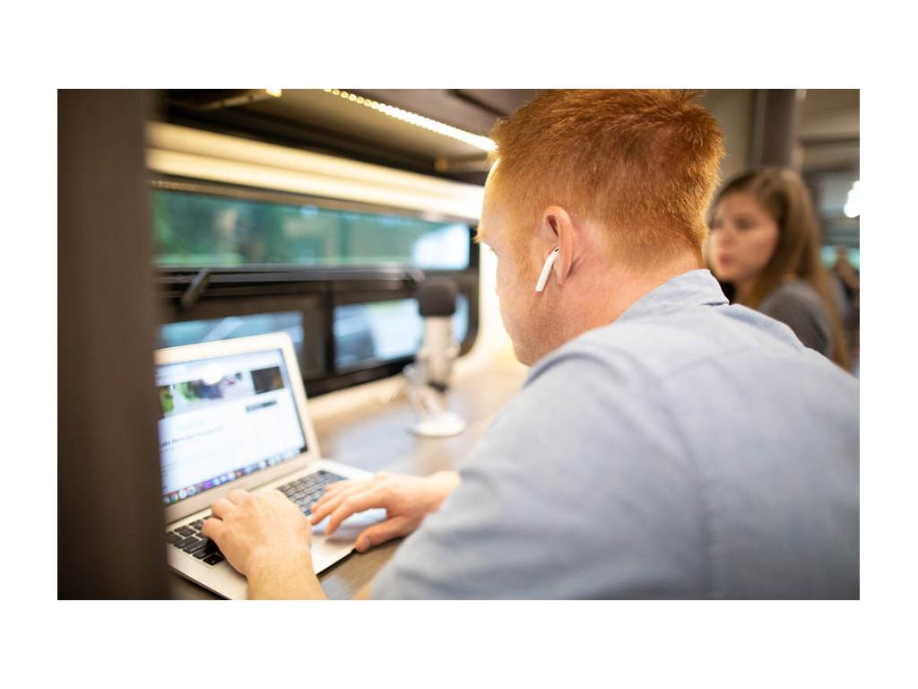 Alyssa and Heath working at work station in RV. Heath is wearing wireless headphones