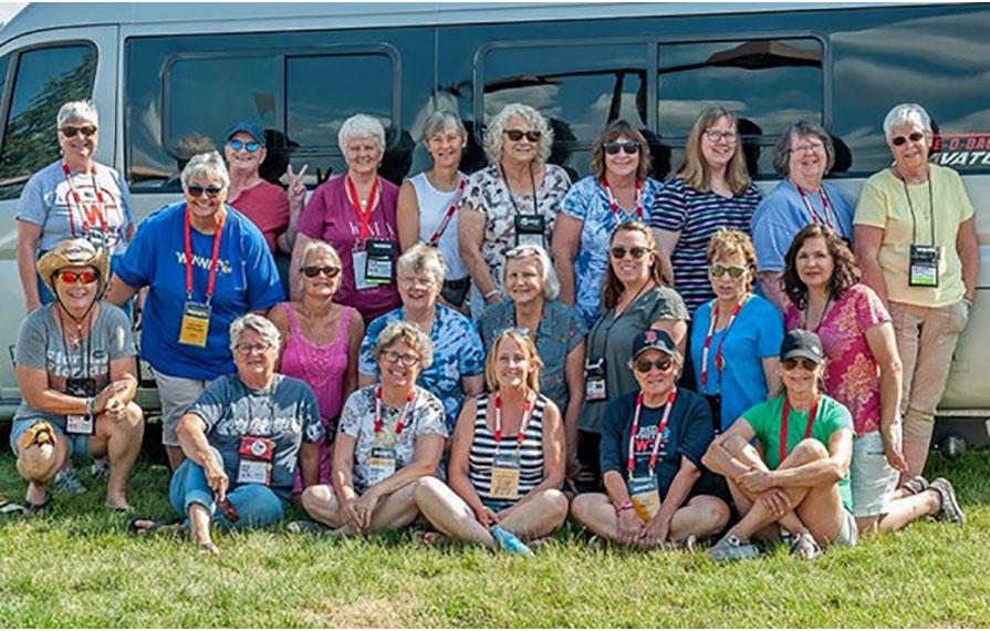Large group of solo ladies huddled in front of a Travato during the Grand National Rally