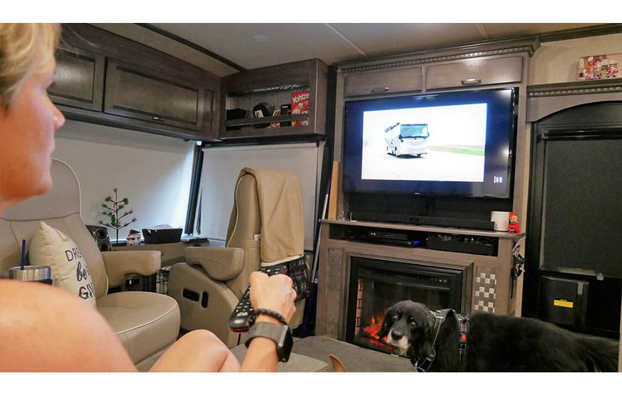 Lin sitting on couch hold television remote with Brady on the floor looking at camera