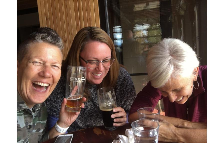 Noel, Jenny Van Atta and Chris all laughing while enjoying drinks at a table.
