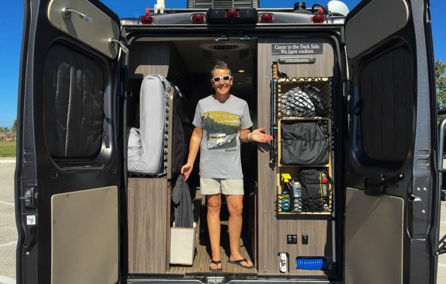 Noel standing in the back of the Travato with the rear doors open showing their modification of added storage