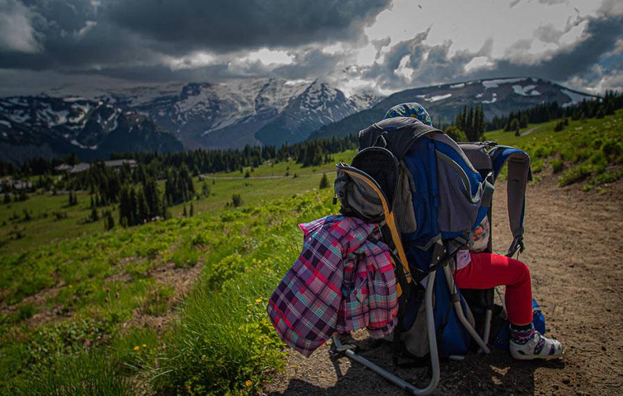 Hiking backpack on the ground with one of the kids and mountains in the background