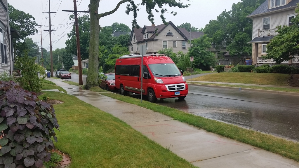 Red Winnebago Travato parked on a residential street.