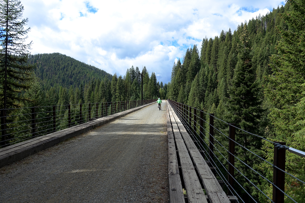 Biker crossing a bridge surrounded by tree covered valley and mountainsides. 