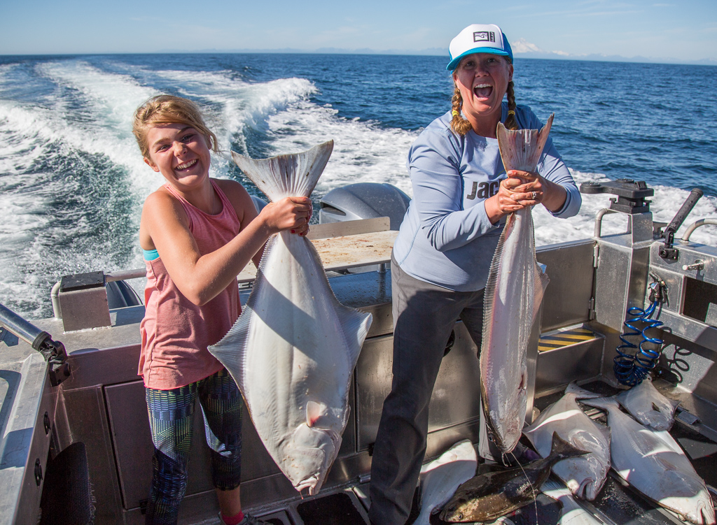 Two ladies on the boat holding massive halibut.