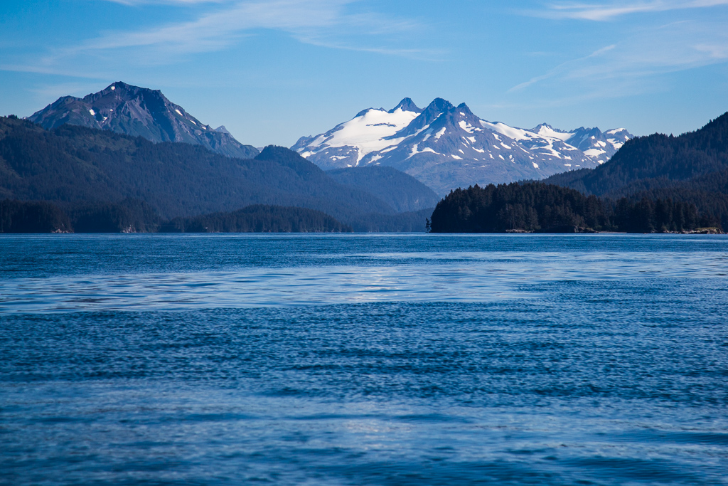 Blue ocean and snow capped and tree covered mountains.