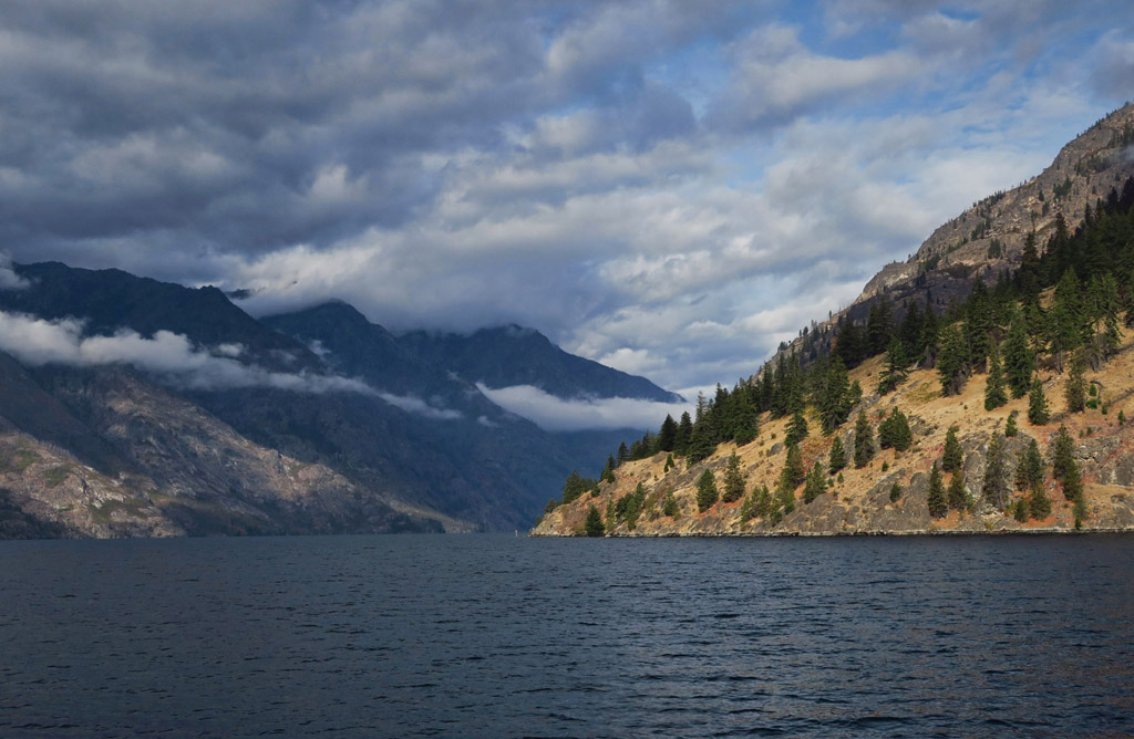 Clouds between mountains at the far end of a body of water.
