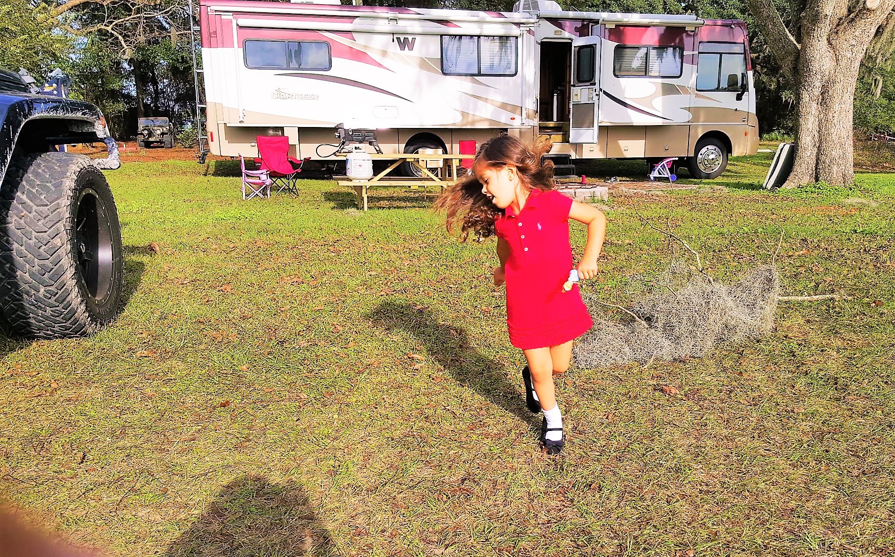 Little girl running in the grass next to a Winnebago sightseer.
