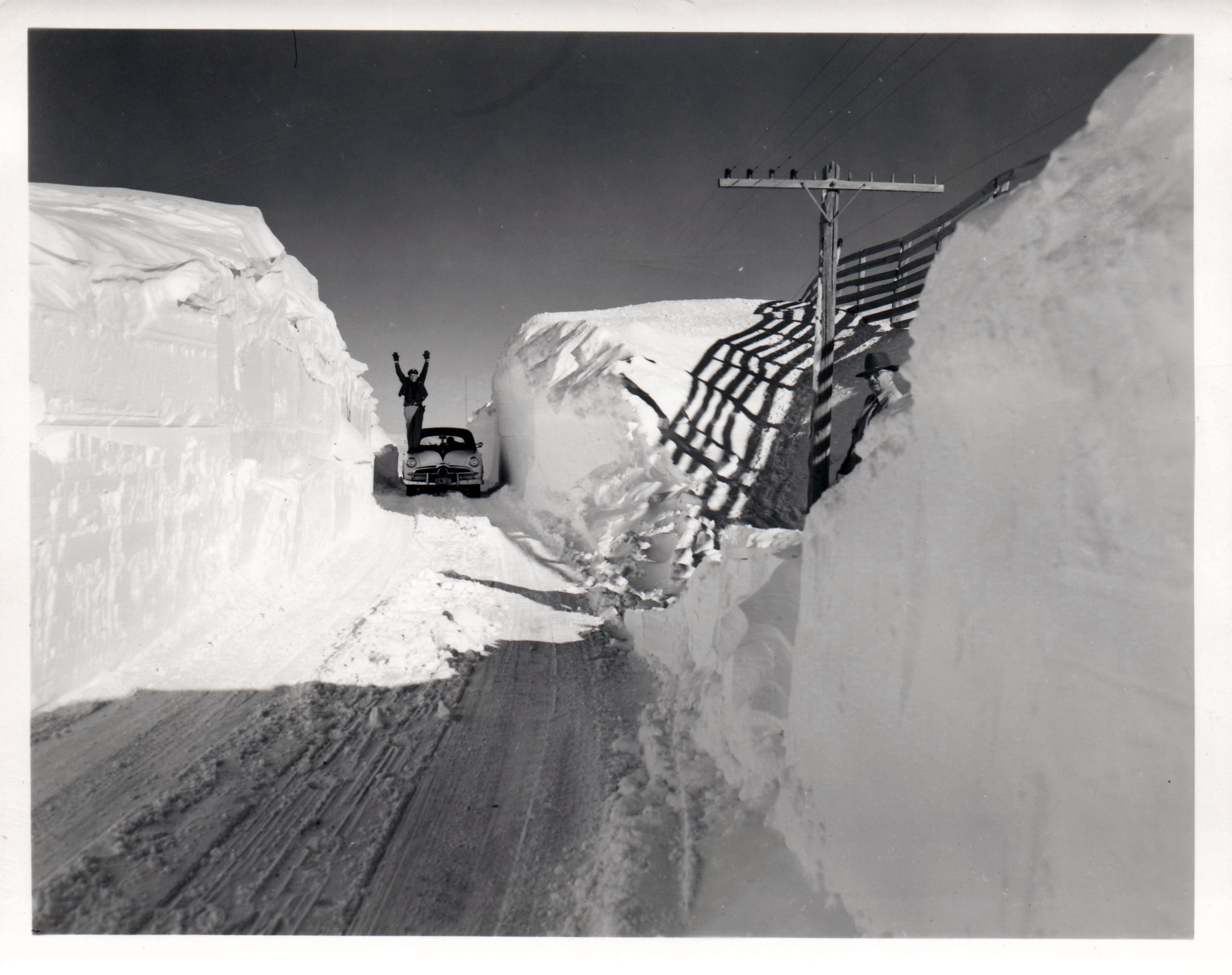Snow piled taller than a car and man standing with his arms raised in the air.