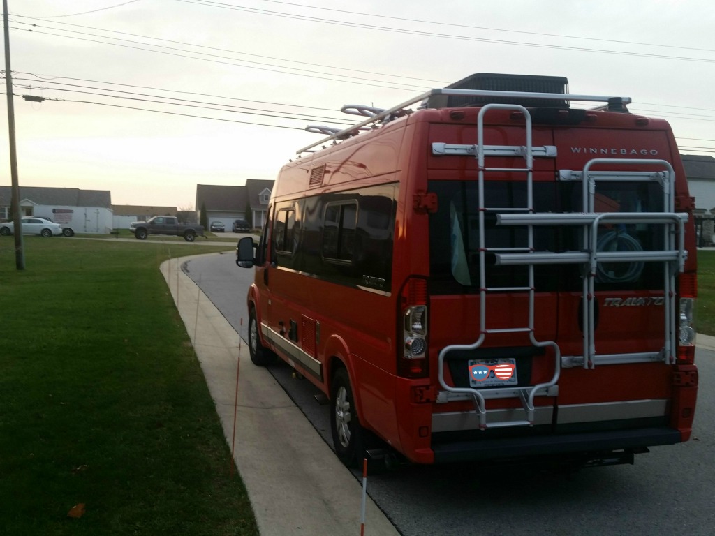 Winnebago Travato parked along the side of a residential street.
