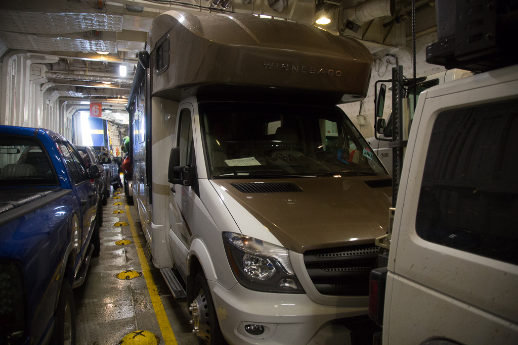 Winnebago View with trailer attached squeezed among other vehicles on the lower level of the ferry.