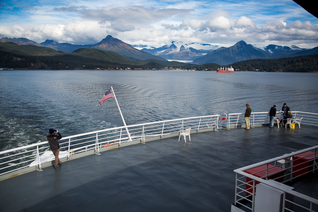 People standing at the back of the boat taking in the mountain covered scenery.