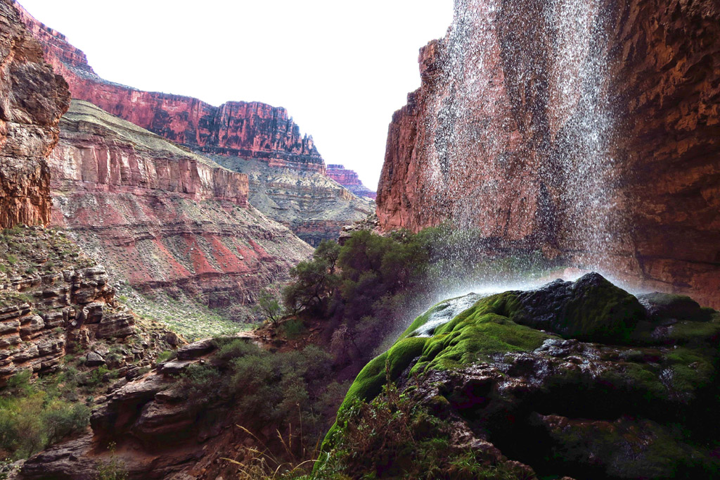 Waterfall pouring down on to moss covered rocks with canyons towering either side.