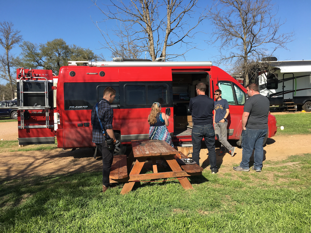 Group of people gathered outside red Winnebago Travato.