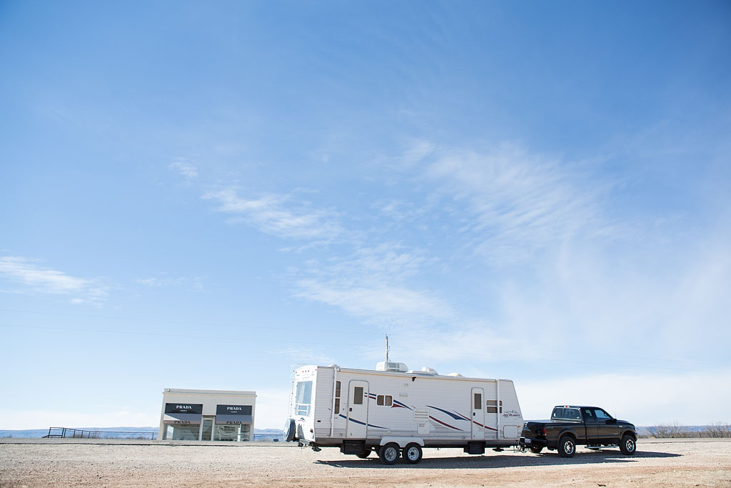 Truck hauling travel trailer parked outside Prada store art exhibit.