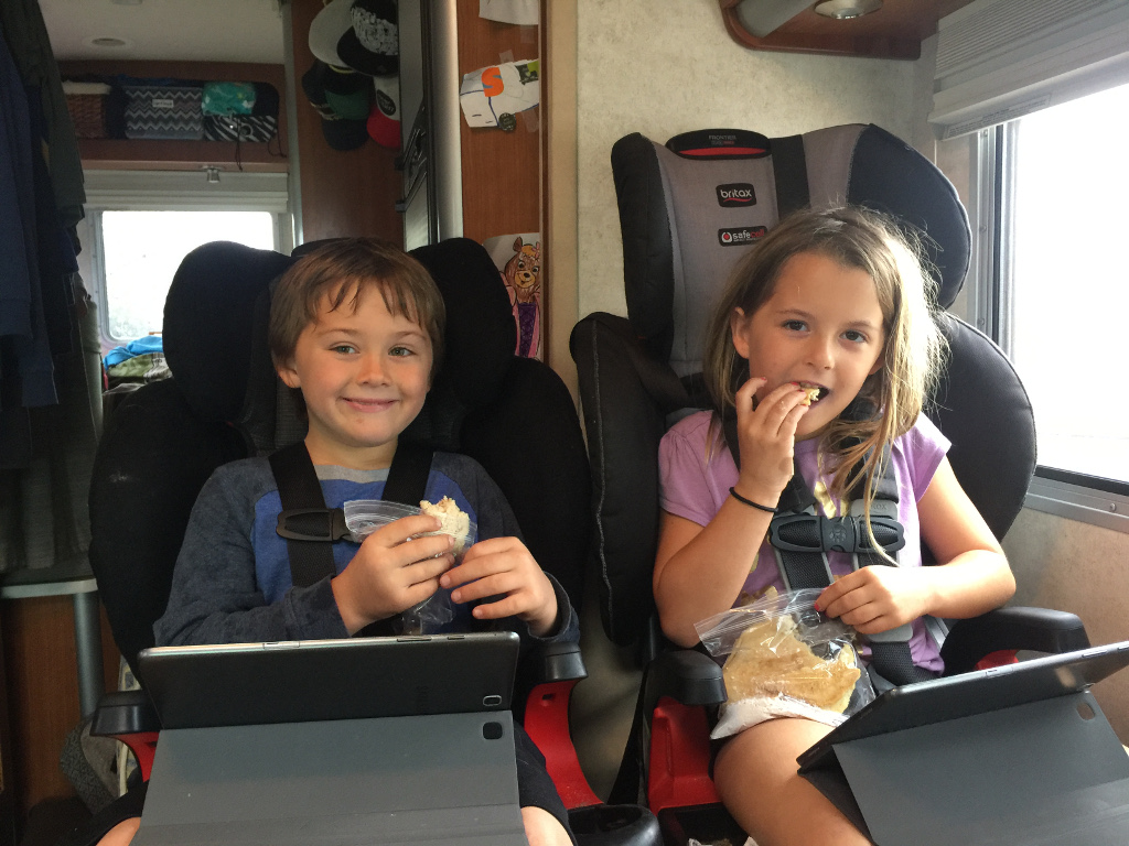 Two kids in car seats watching something on a tablet.
