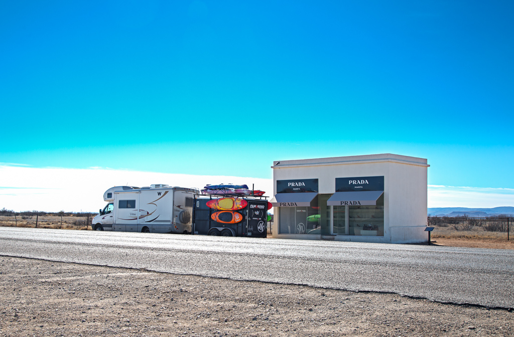 Winnebago View with trailer attached parked next to a stand alone Prada store in the middle of nowhere.