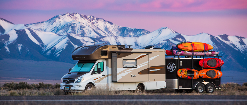 Winnebago View with trailer attached parked on the side of the road with mountains in the background.