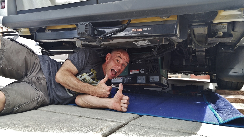 James laying on the ground with a smile and thumbs up underneath Winnebago Travato.