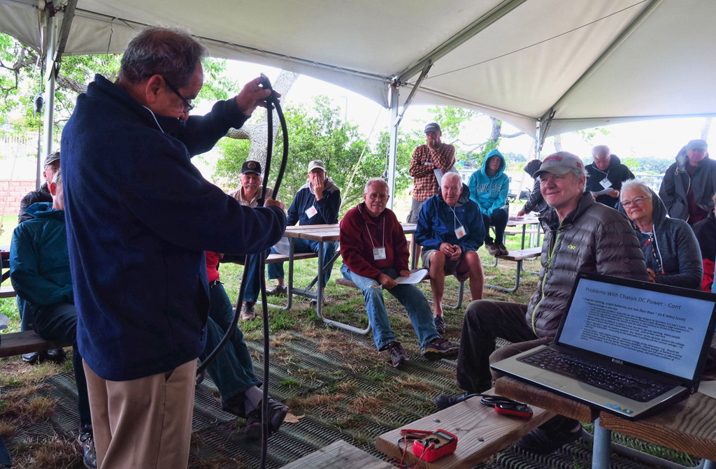 Vendor giving a talk on electrical system to a group of rally attendees.