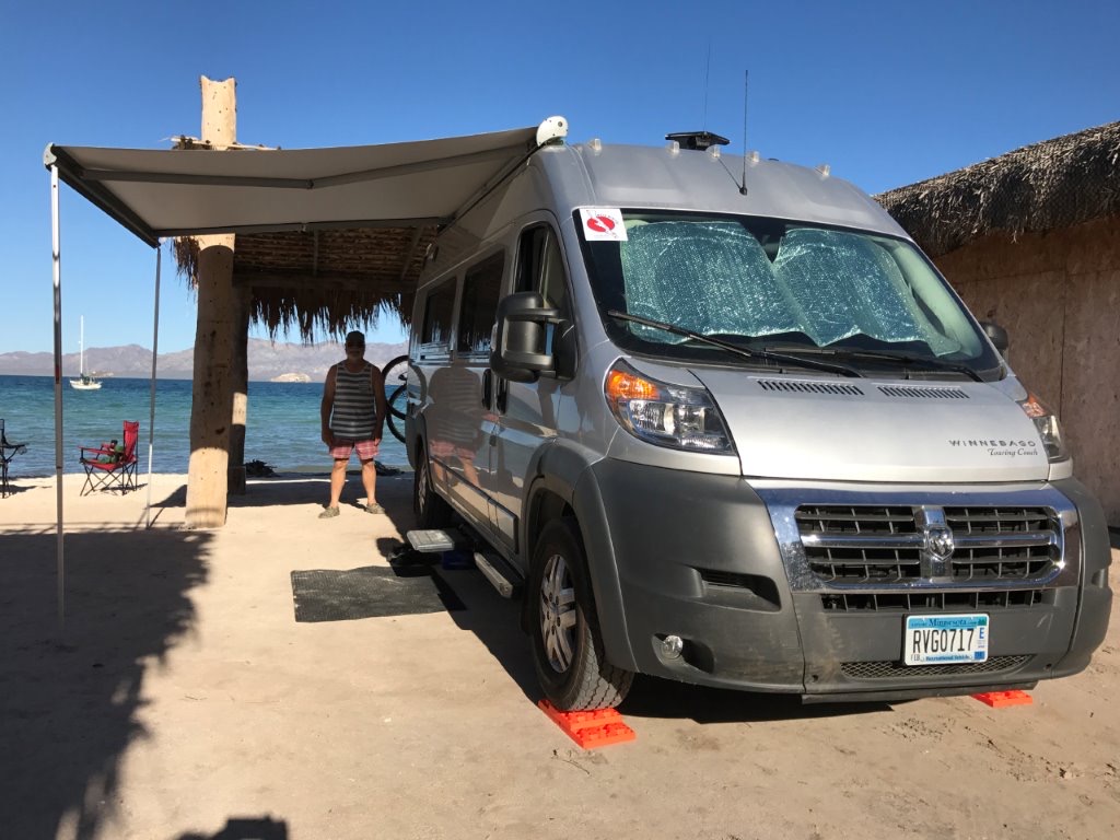 Winnebago Travato parked at campsite right next to the ocean.