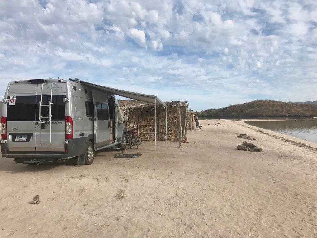 Winnebago Travato parked on the beach right next to the water.