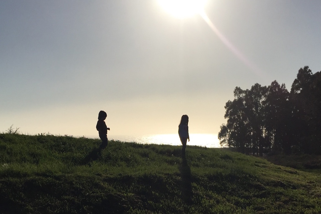 Silhouette of two kids walking along hillside with sun setting behind them.
