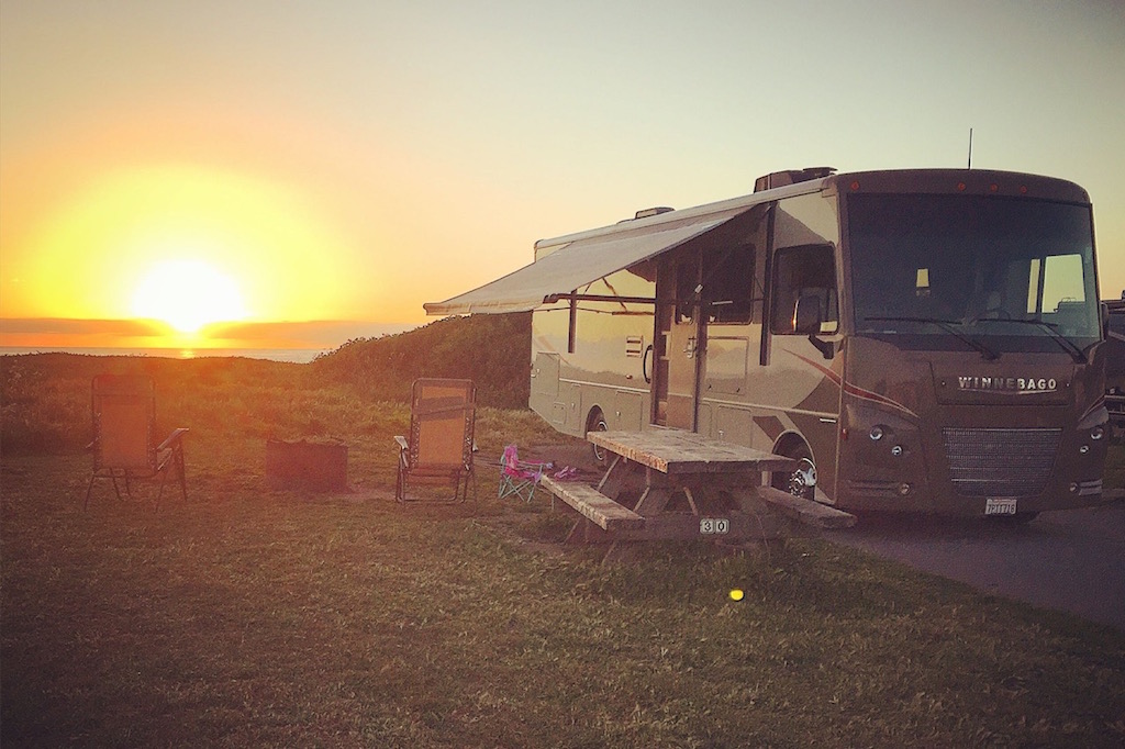 Winnebago Vista parked in campsite with picnic table and camping chairs sitting outside it.