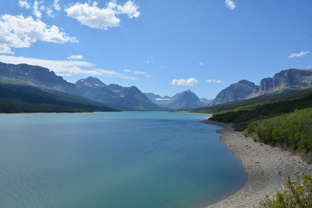 Magnificent blue water of Many Glacier with trees and mountains surrounding.