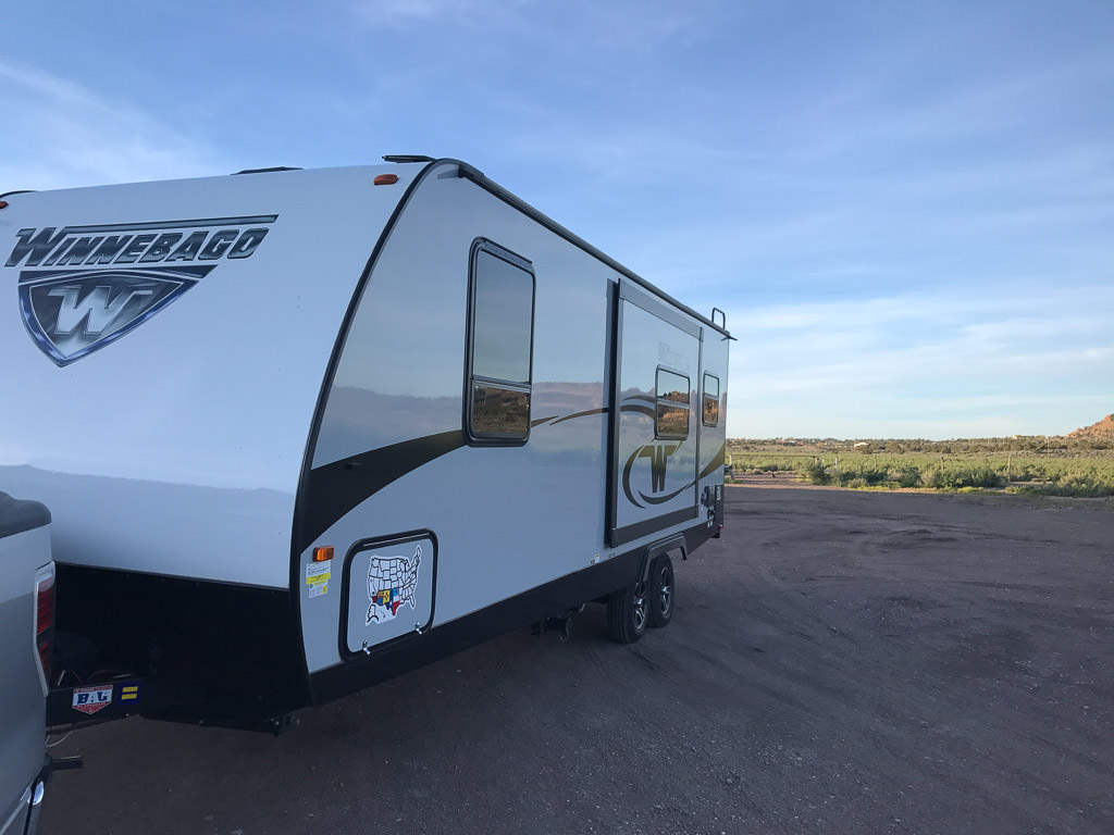 Winnebago Minnie towable parked in dirt lot.