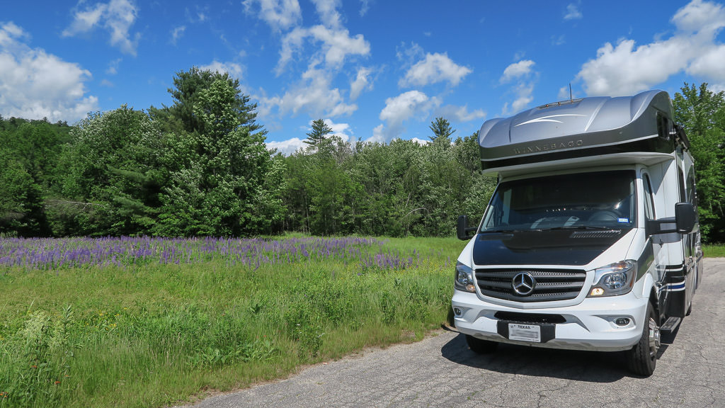 Winnebago View parked on gravel road next to field.