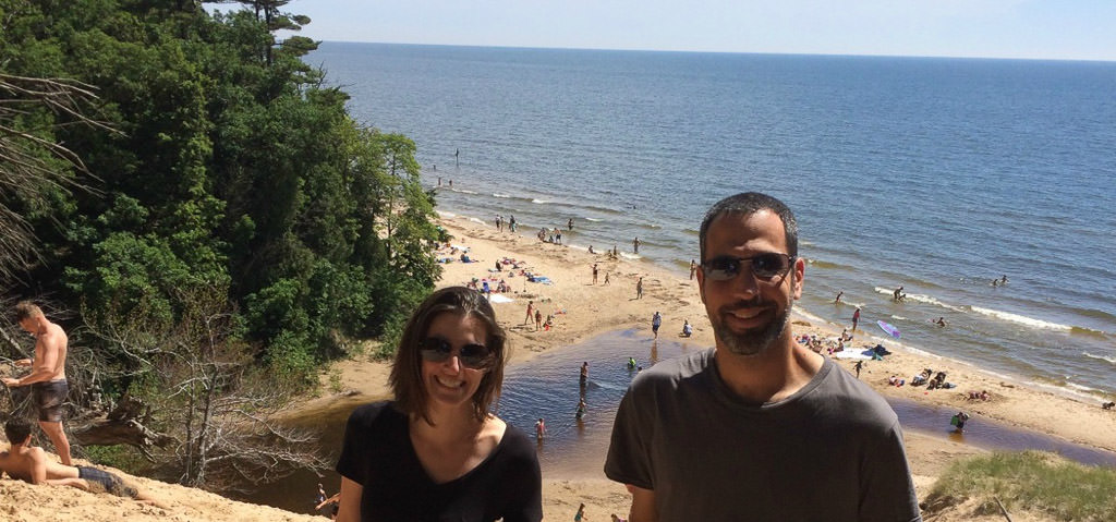 Man and woman standing with crowd of people gathered at the beach below.