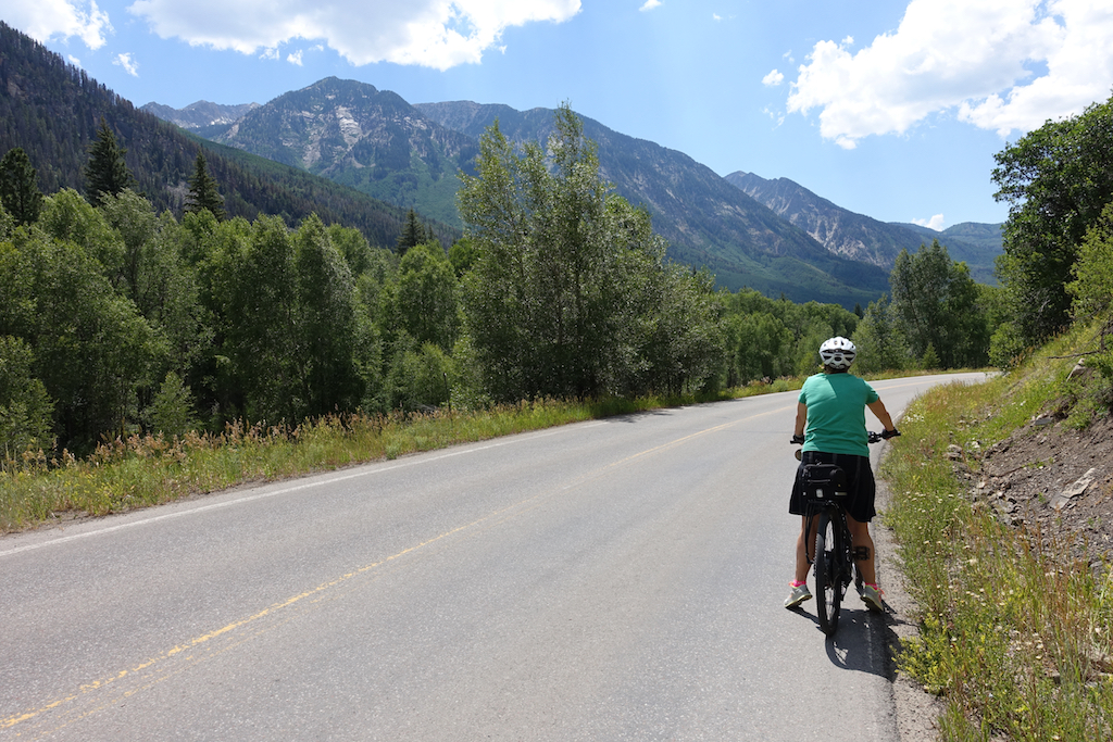 Terry on her bike stopped on the side of the road with mountains lining the way.