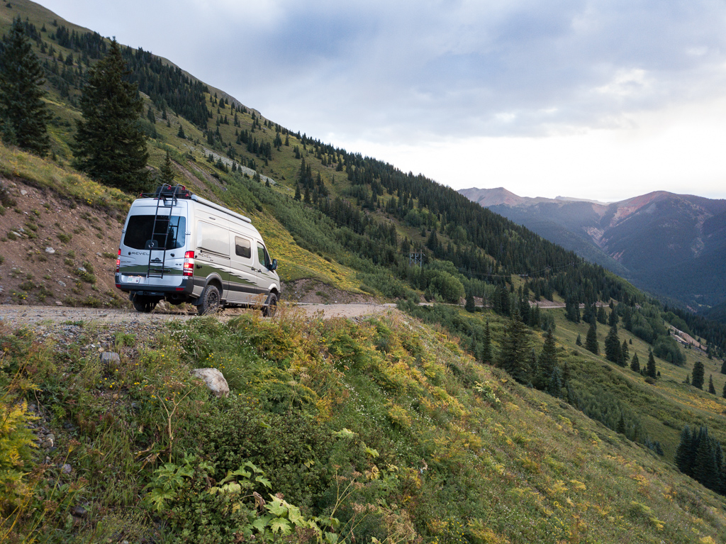 Winnebago Revel parked on narrow hillside dirt road leading to mountains.