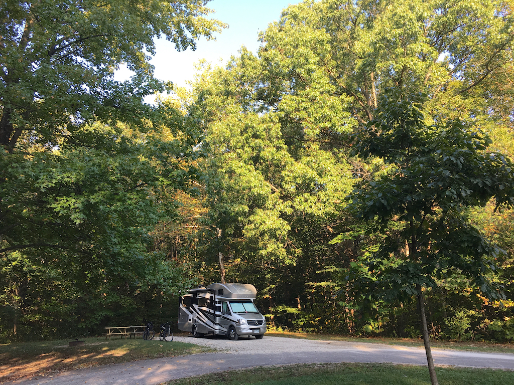 Winnebago Navion parked in tree surrounded campsite