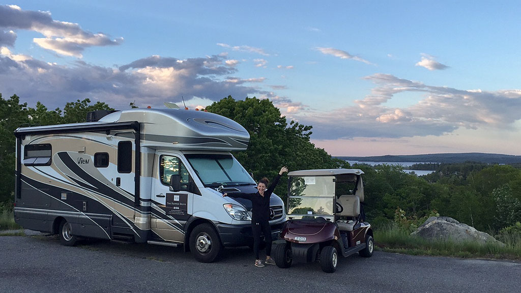 Brittany standing by Winnebago View and a golf cart with water in the background.