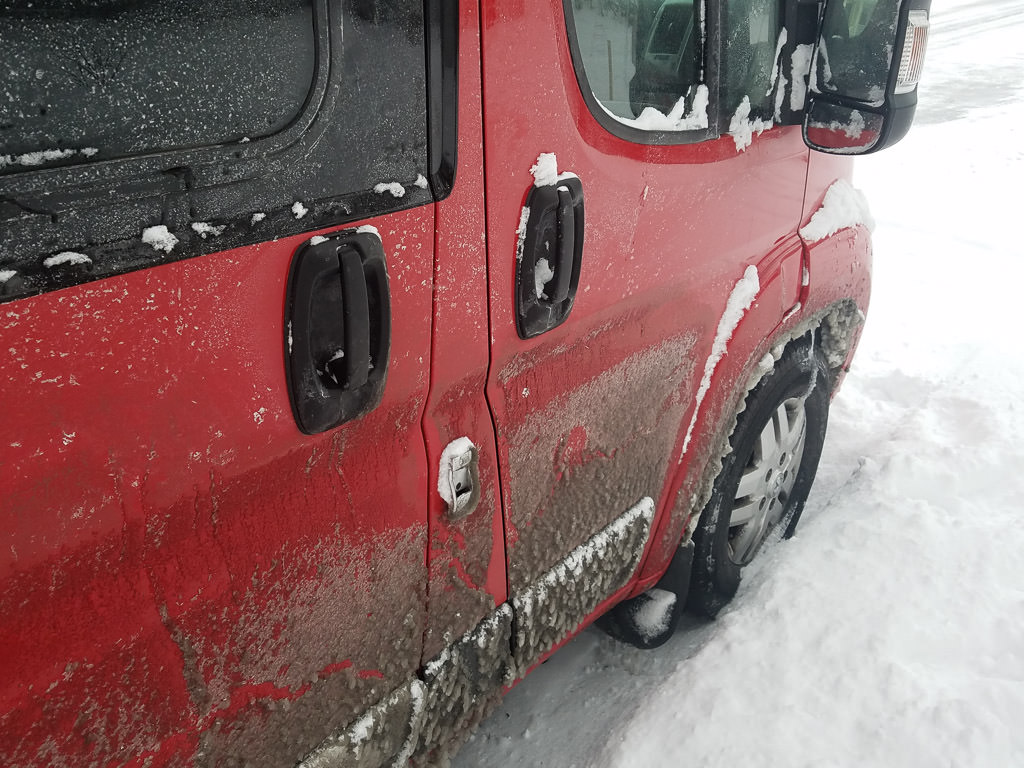 Winnebago Travato sitting in a few inches of snow with ice covering the side