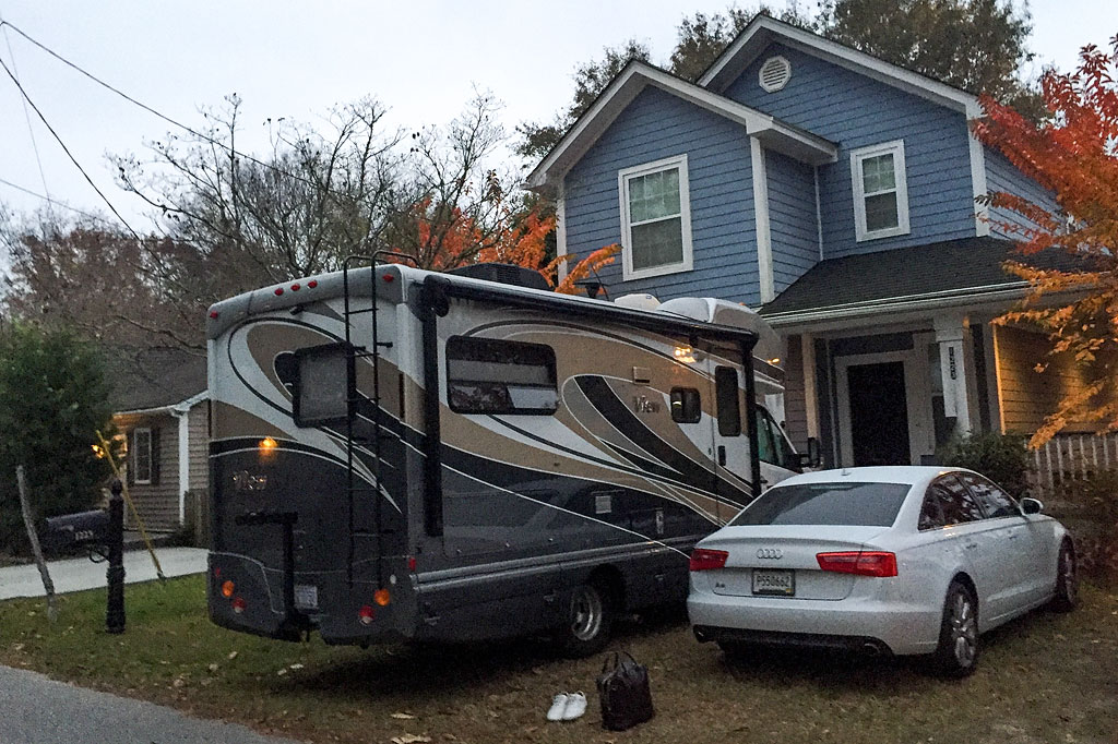 Winnebago View and car parked in front of a blue house surrounded by trees