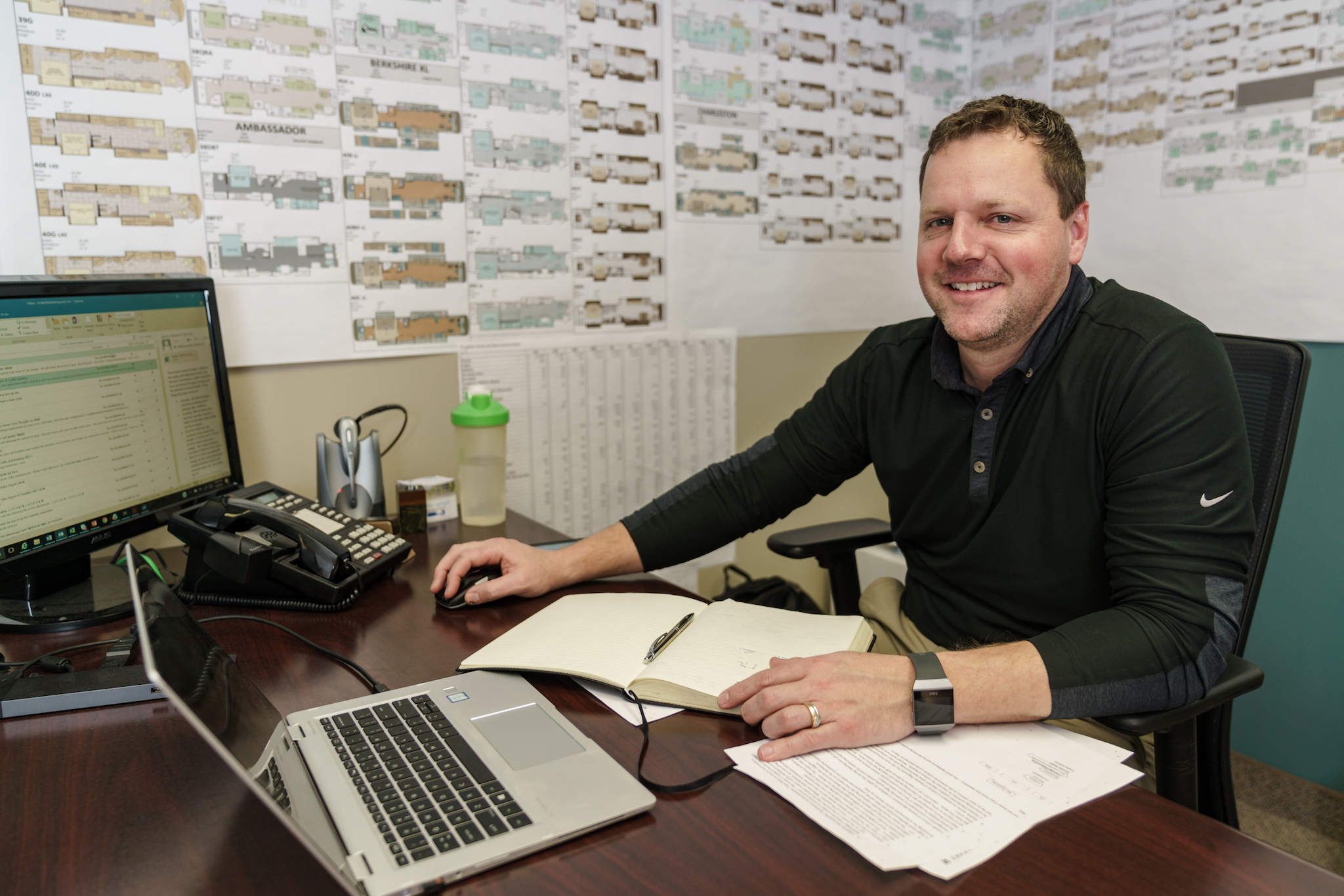 Ryan Roske working at desk with dozens of floorplans mapped on his walls.