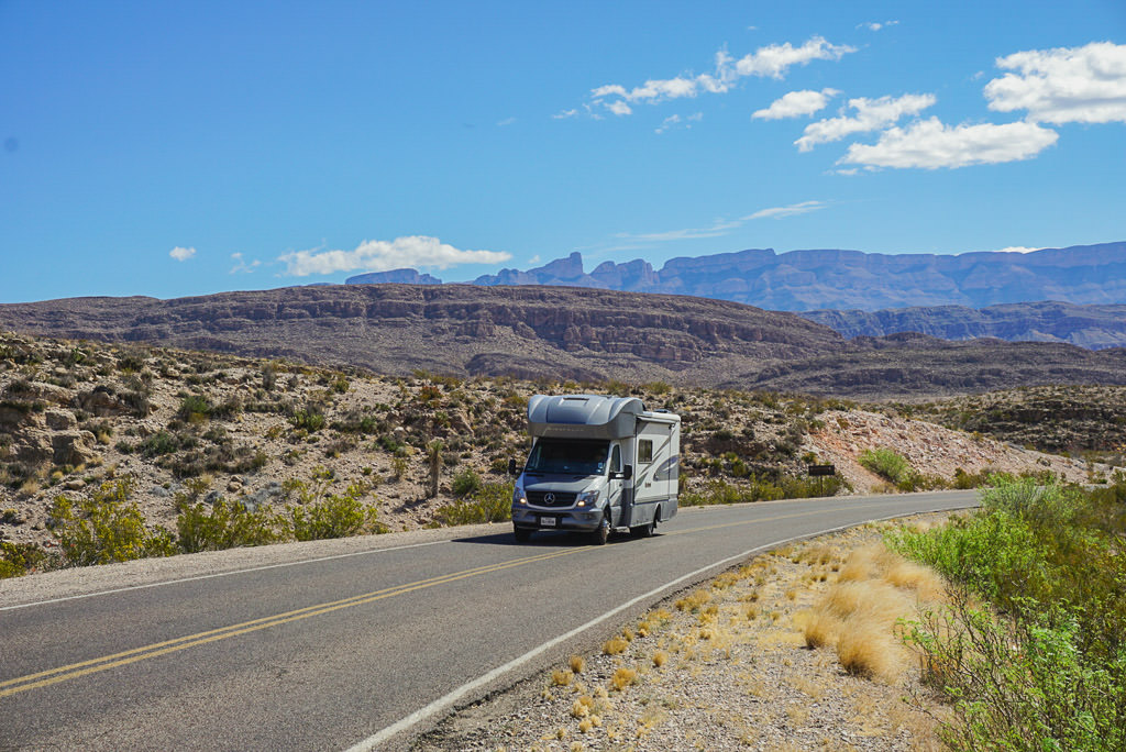 Winnebago Navion driving along road with rough terrain surrounding